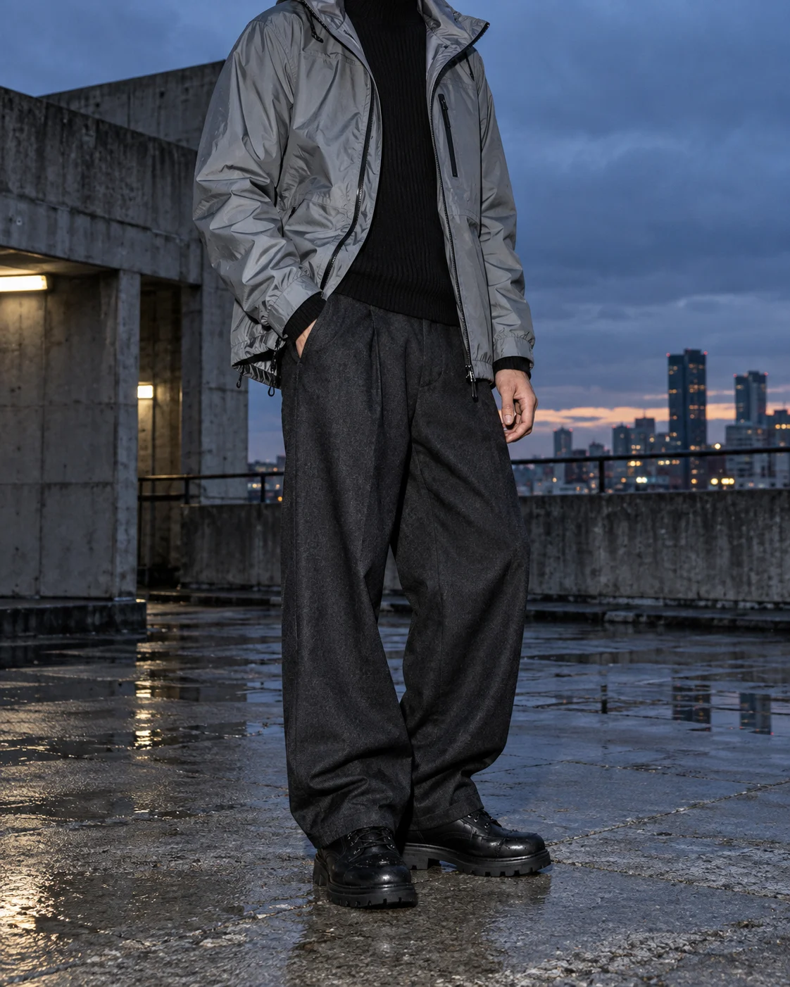 Neck-down model wearing a silver technical shell and wide charcoal trousers on a wet rooftop
